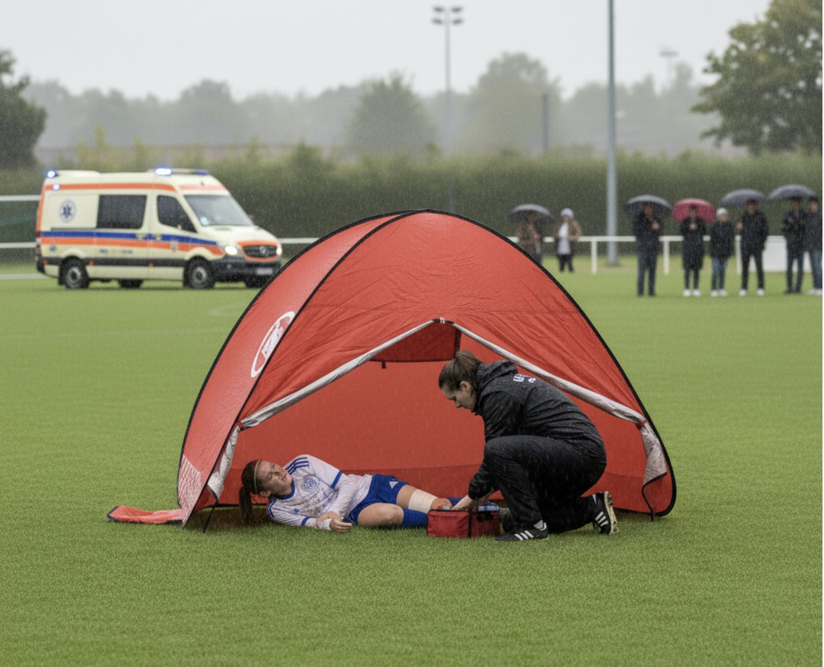 InciTent deployed on a rain-soaked pitch, sheltering an injured player as a physio treats her, with an ambulance arriving